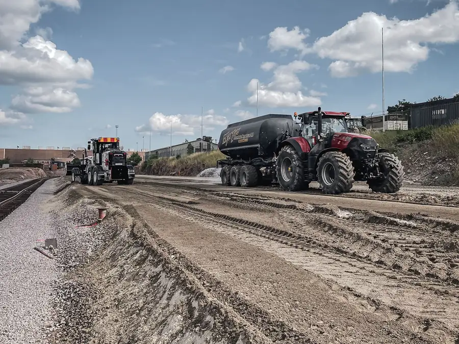 Traktor med vattentank och väghyvel från Hjerpes Maskincentra på en stor yta som stabiliseras, intill ett järnvägsspår